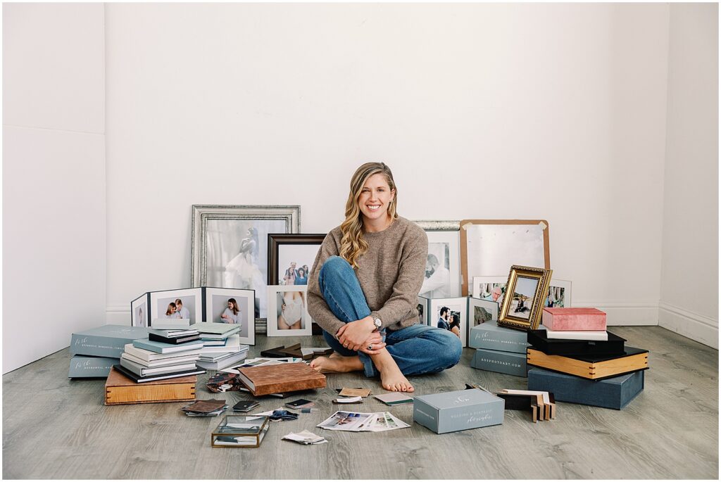 Amandarose, owner of AGS Photo Art, sits surrounded by albums, pictures, frames, folios, and design swatches.