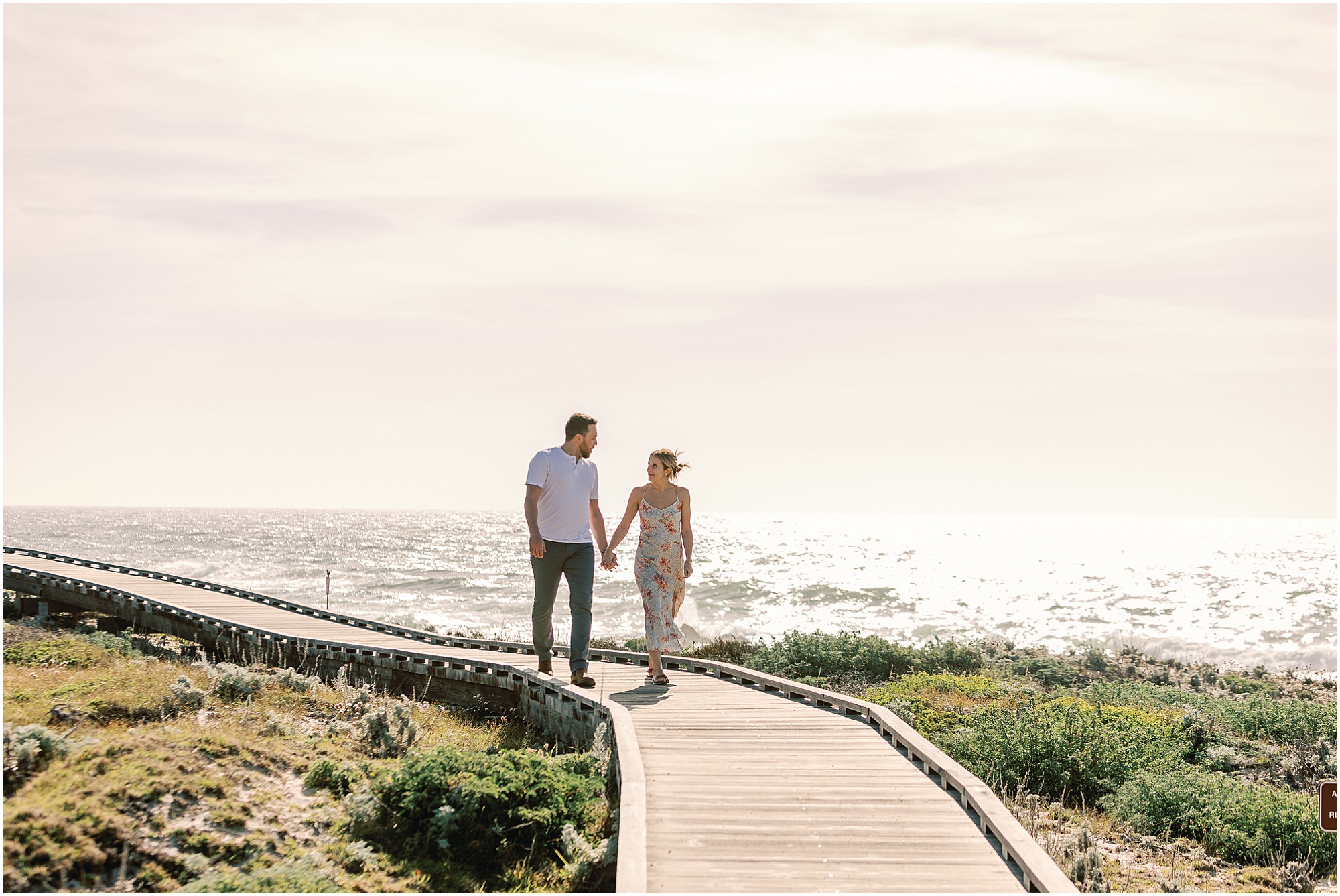 Asilomar Beach Proposal Photographer captures Josh and Tasha walking hand in hand along the Pacific Grove boardwalk at sunset.