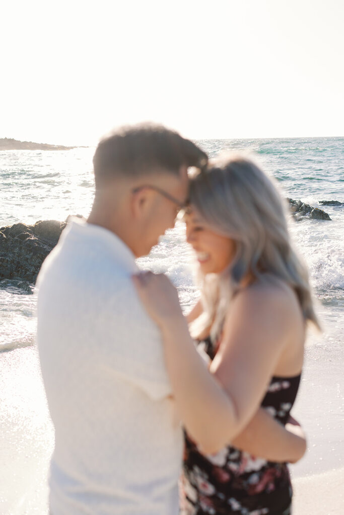 Artistic photo of Mark and Vivian slightly out of focus, with the sparkling Spanish Bay ocean behind them during their Pebble Beach engagement session.