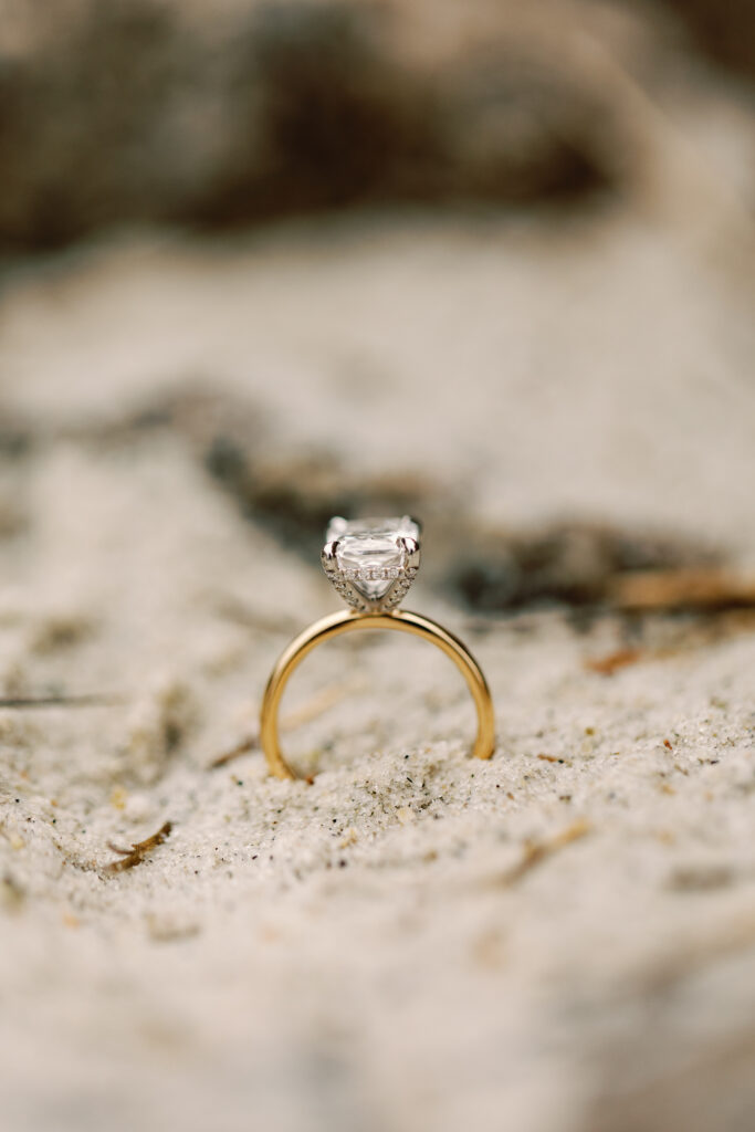 Engagement ring photo with coastal tones in the background and ring in the sand.