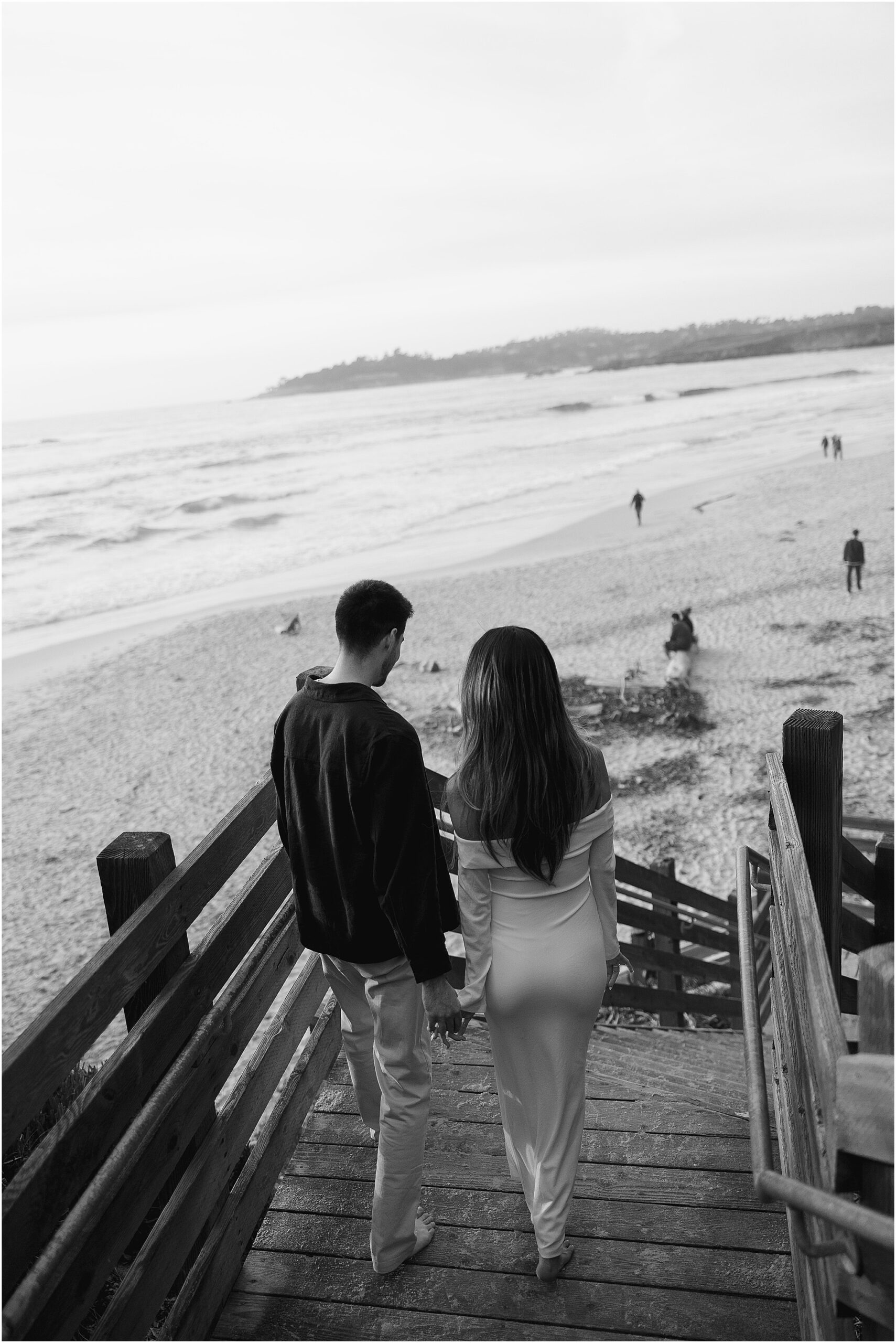 Black and white photo of couple walking down wooden stairs to the beach
