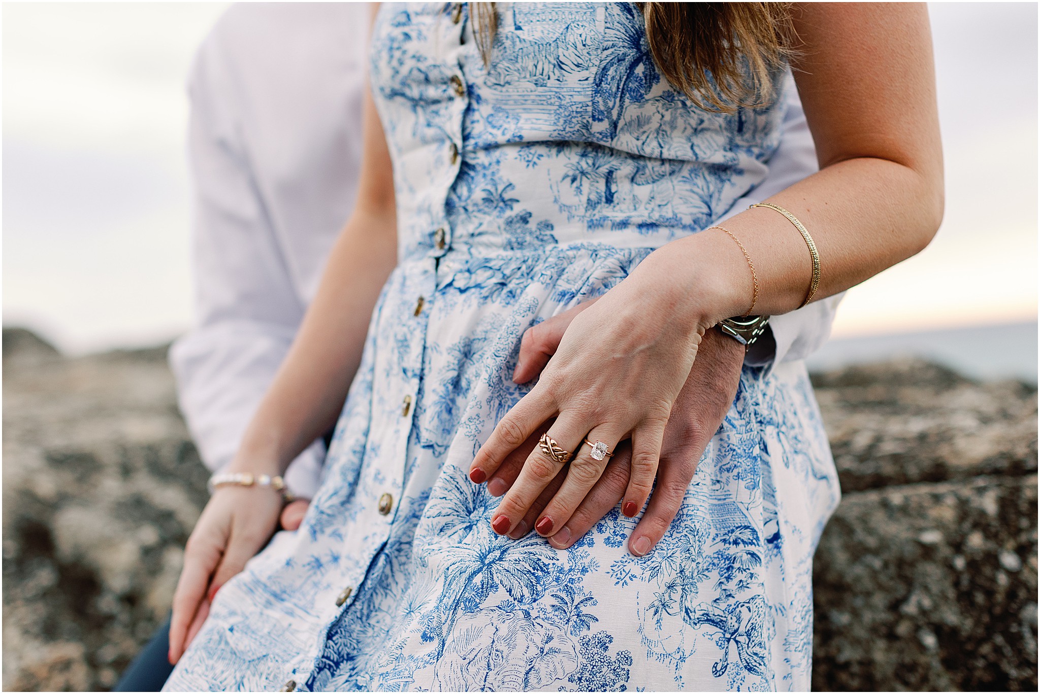 Stylish couple in white and blue outfits posing for engagement photos featuring the ring details.