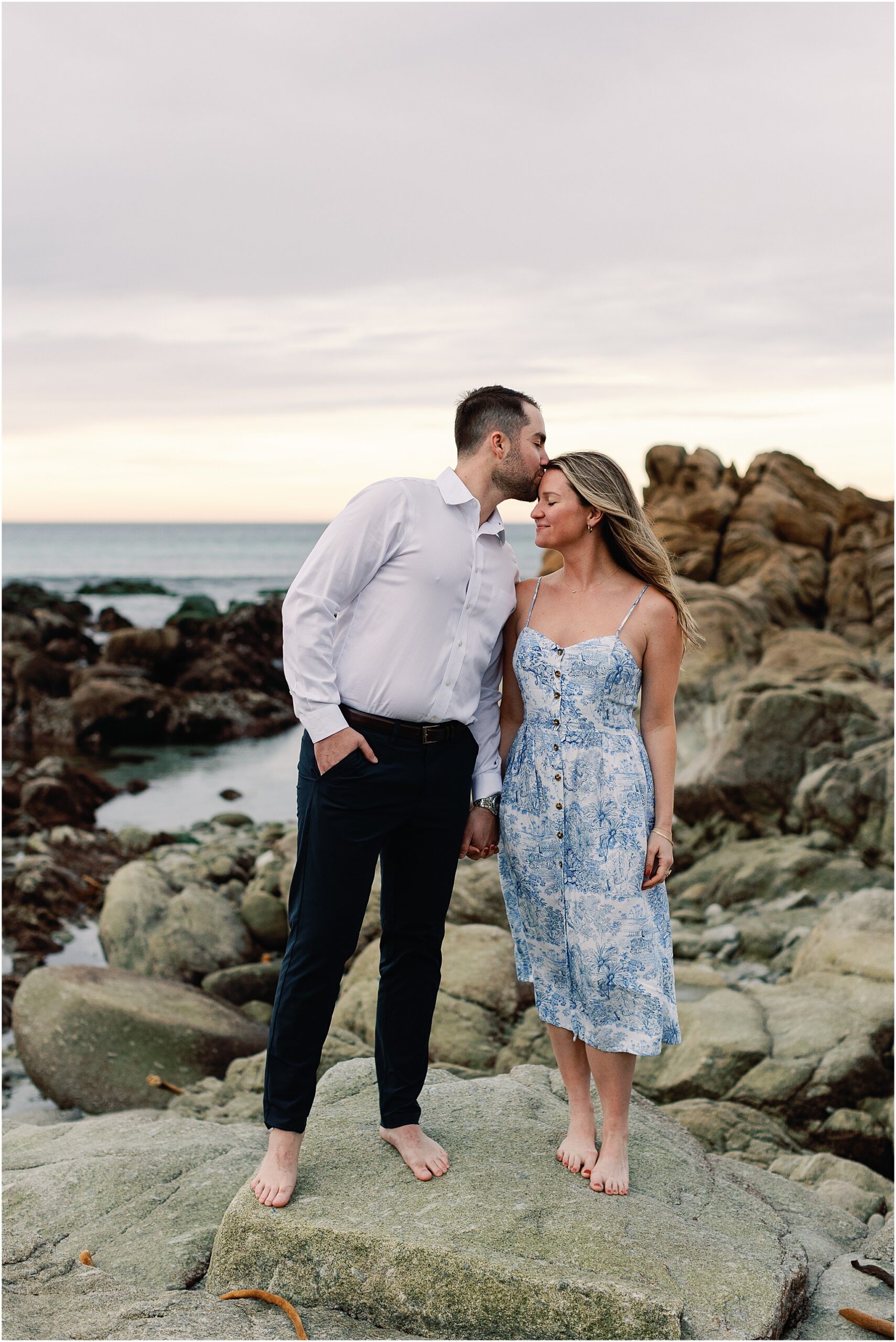 Romantic couple standing on rocky shore during their Pebble Beach proposal.