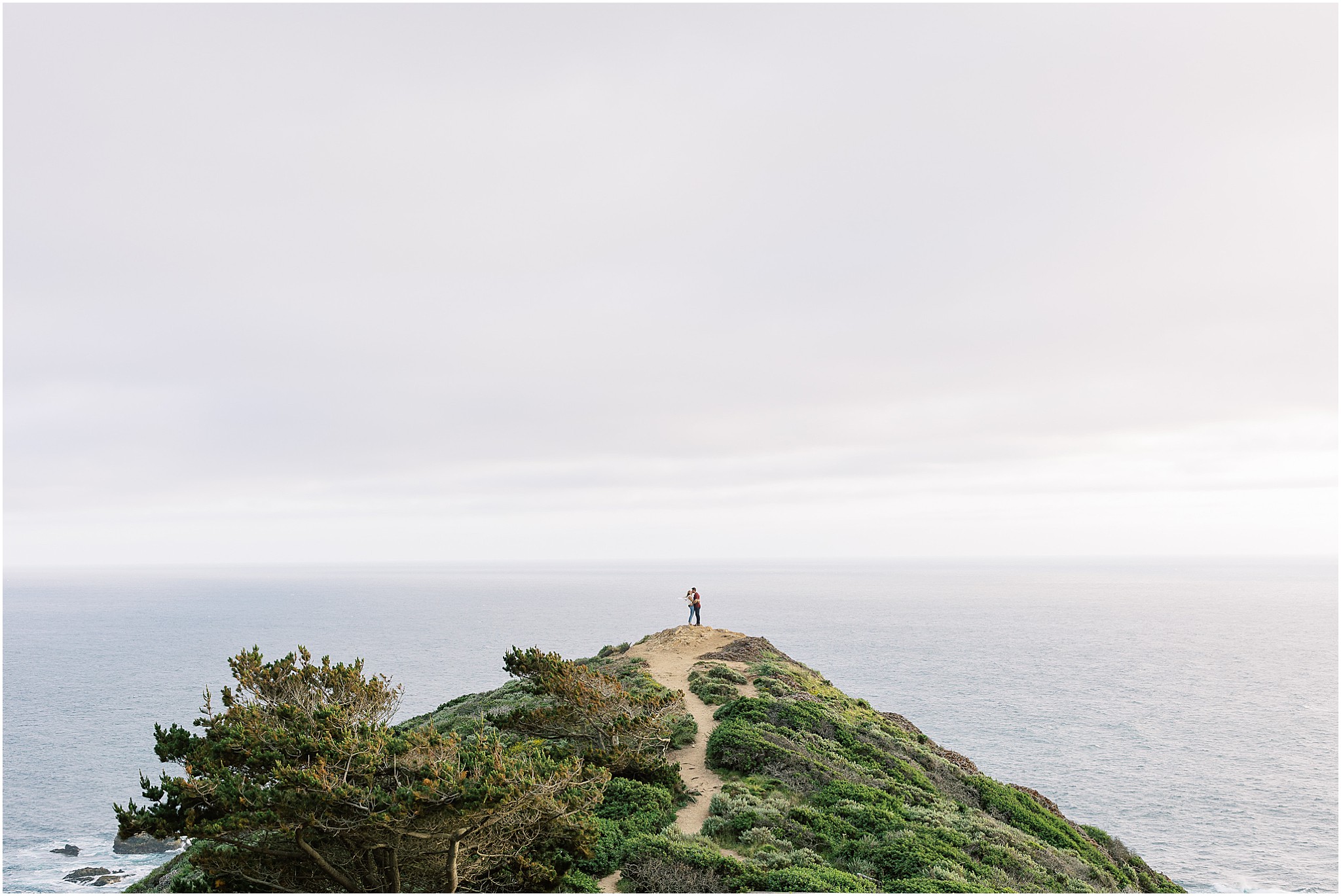 Couple framed by the Big Sur coastline during their romantic engagement shoot