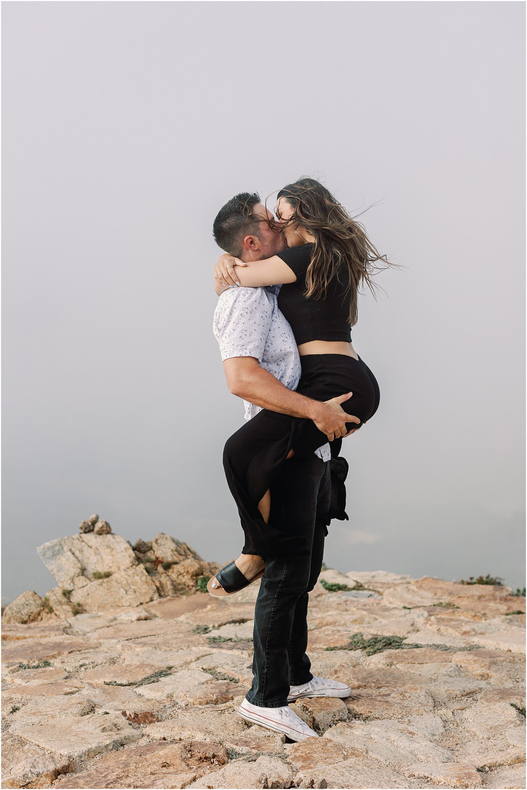Marc and Lauren kissing with dramatic Big Sur coastline behind them.