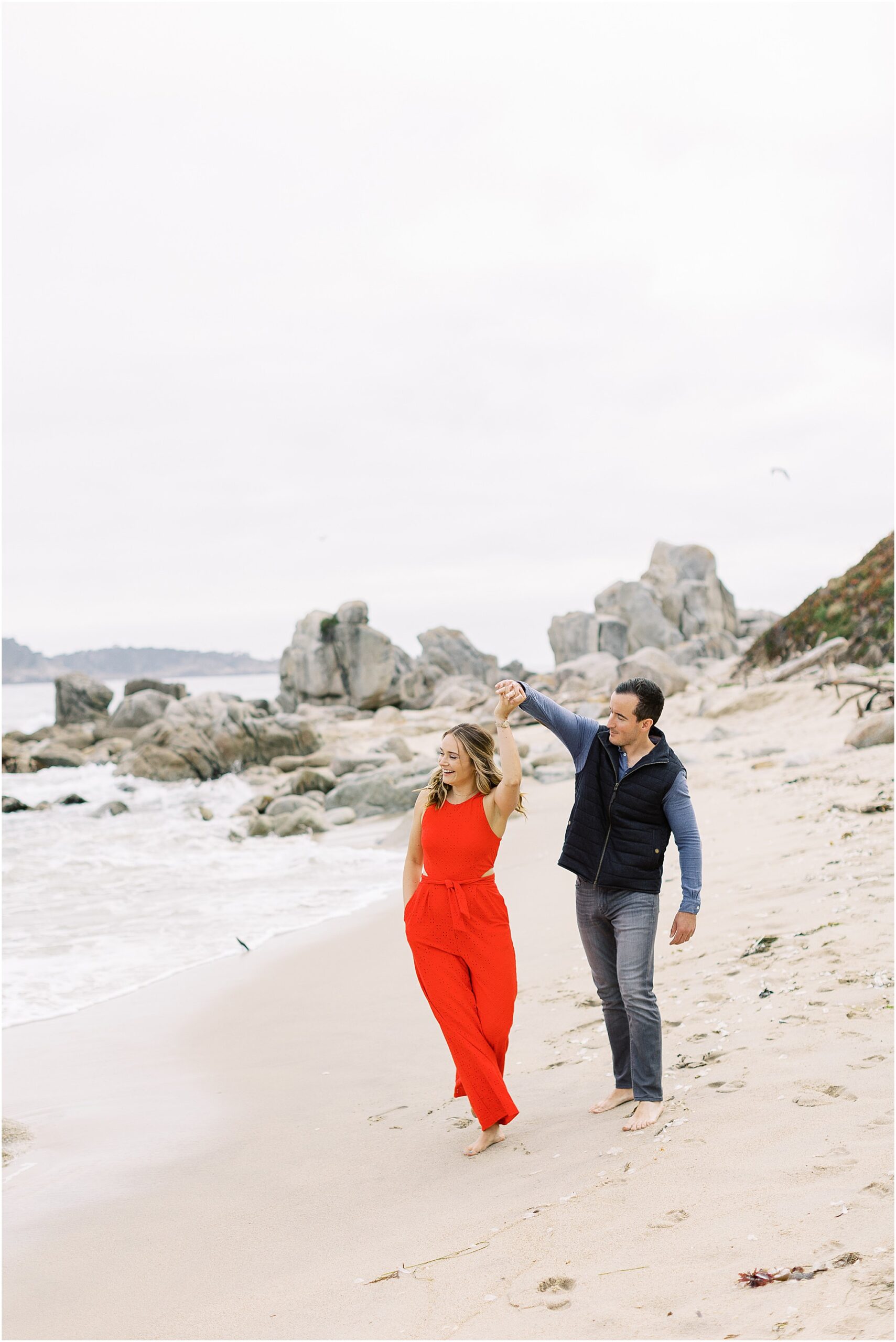 Just engaged couple twirling in the sand with soft coastal light behind them.