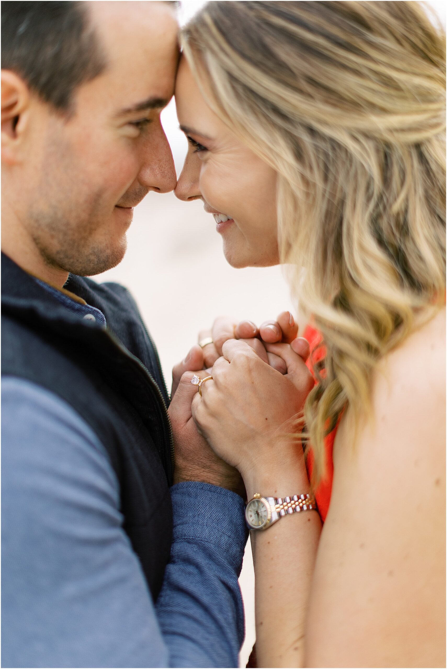Couple standing forehead to forehead with waves rolling in behind them