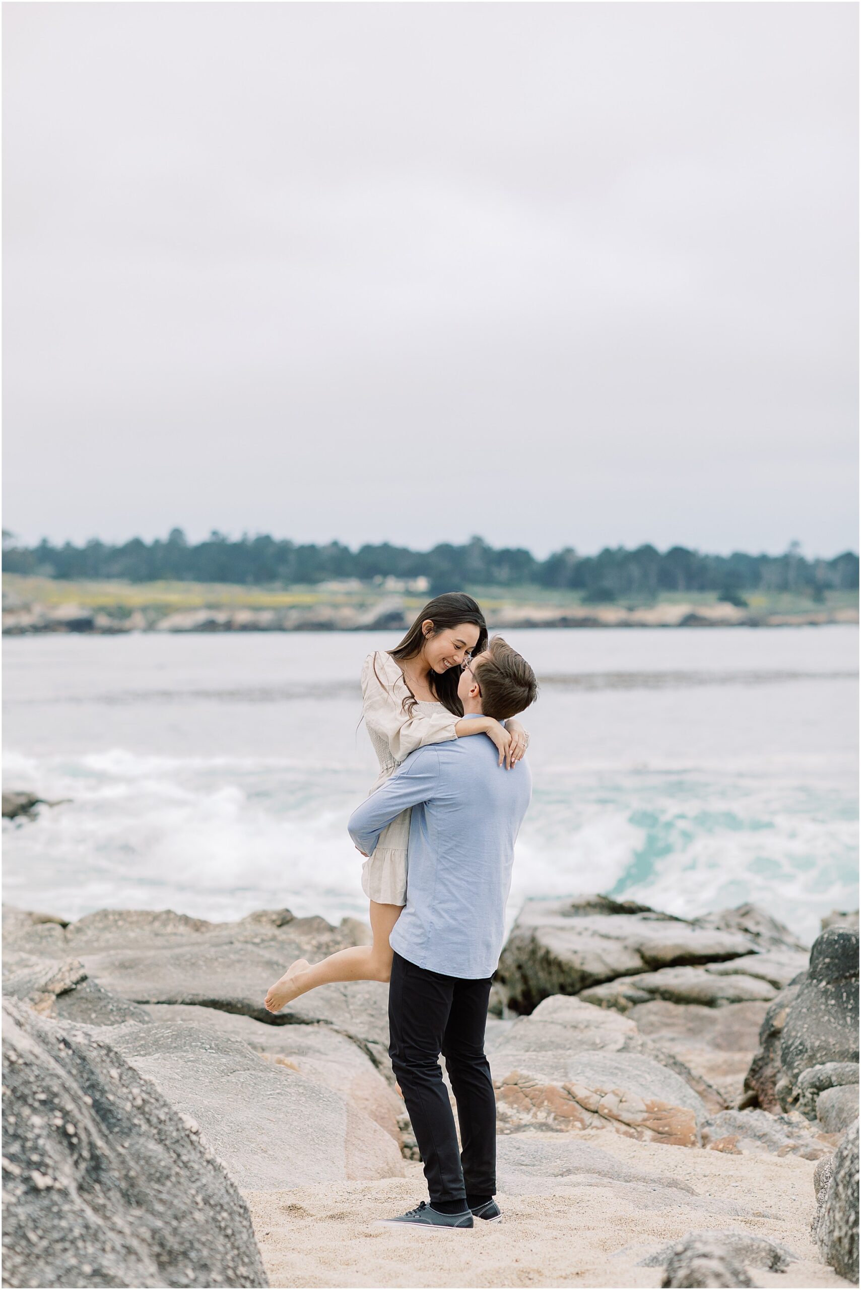 Groom to be holding his bride to be close with the ocean behind them.