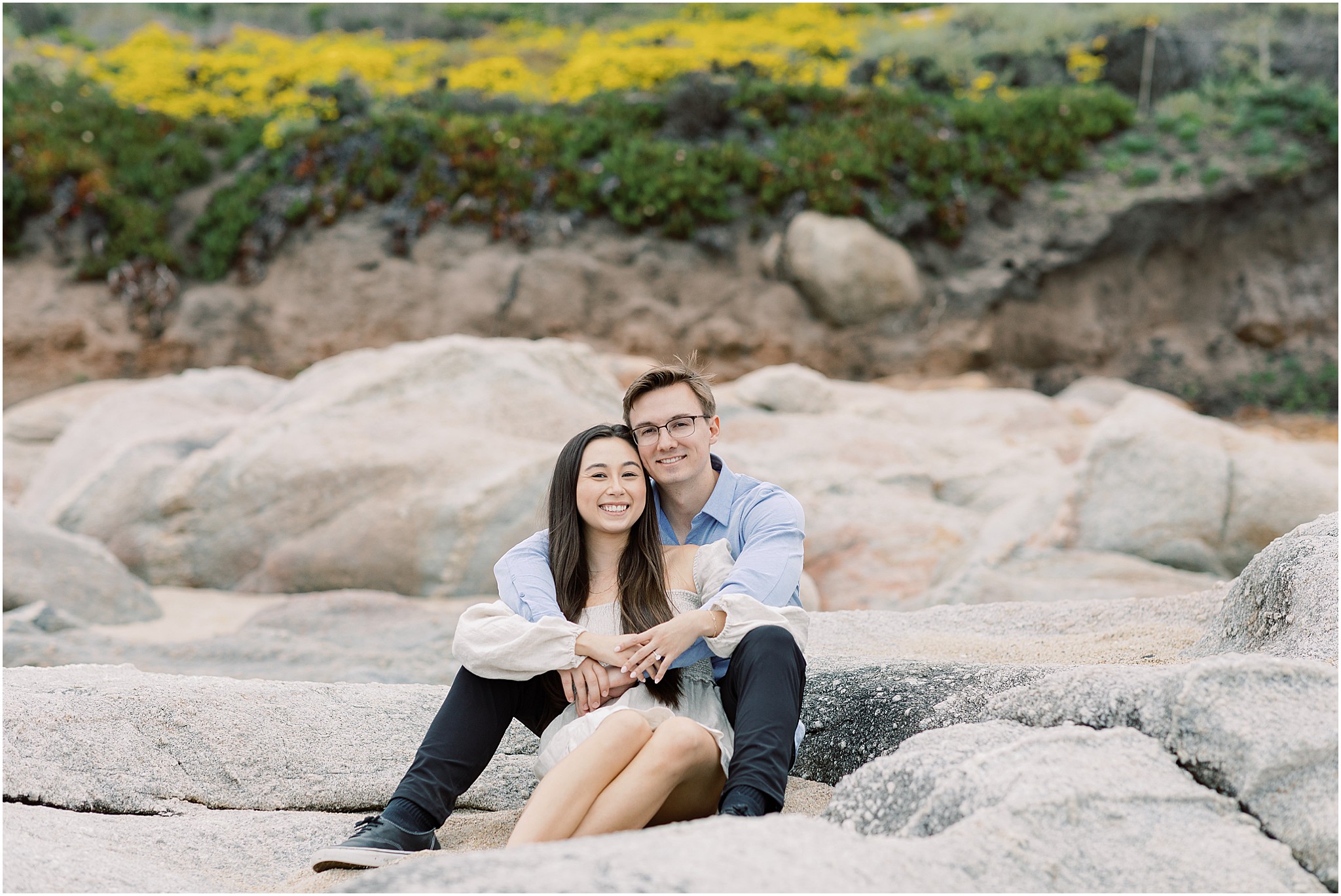 Couple snuggled together on the rocks with waves crashing nearby.