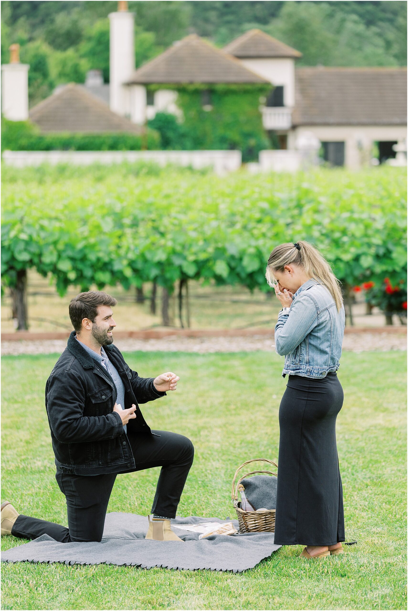 Groom to be kneeling during a Folktale Winery surprise proposal with vineyard views behind them.