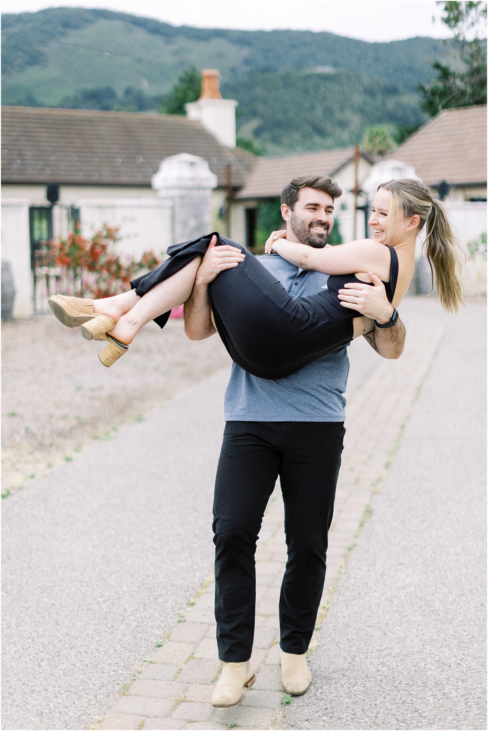 Groom to be carrying his fiancée along a path after their winery proposal in Carmel.