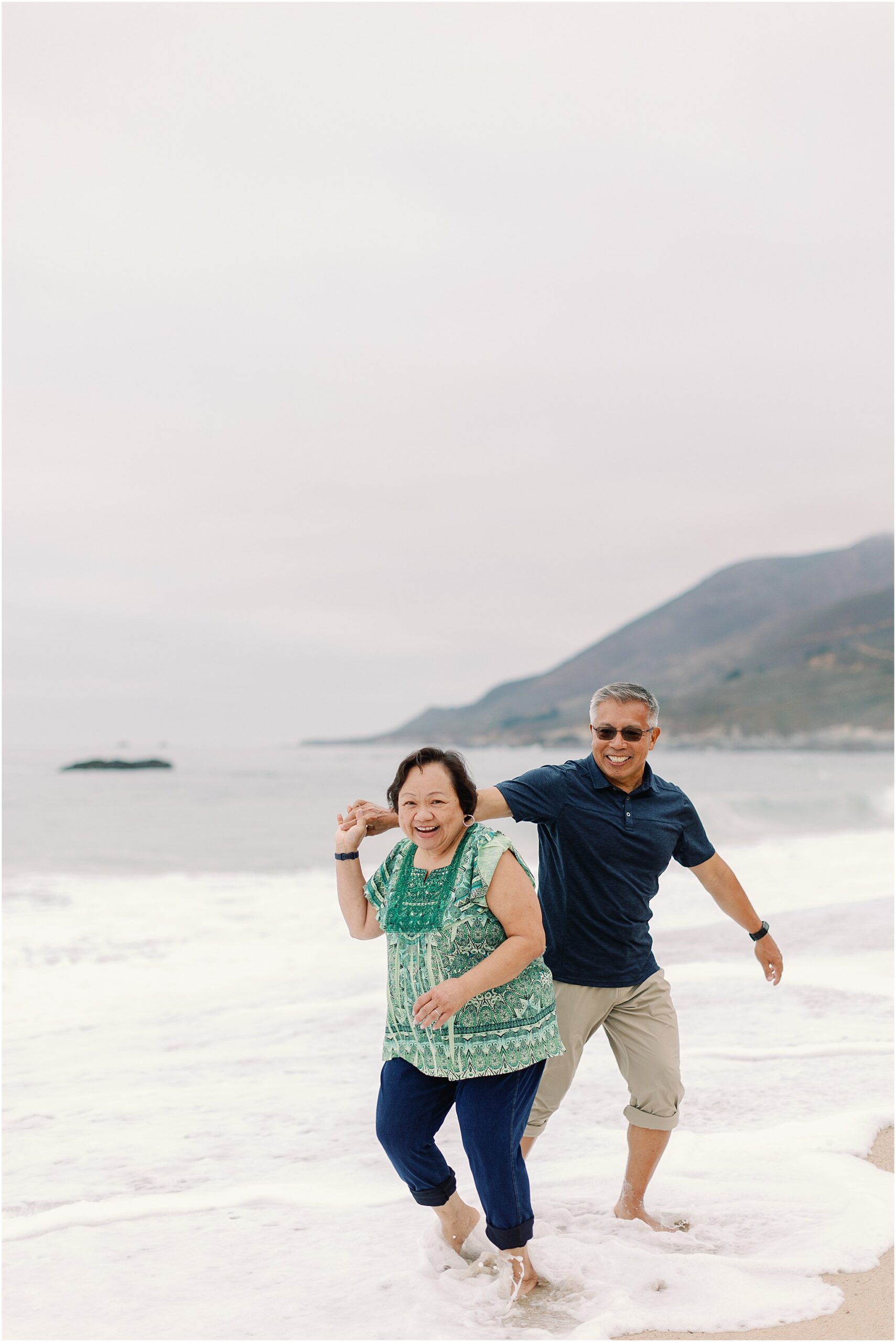 Couple playing in the ocean on the Big Sur shoreline with waves in the background.