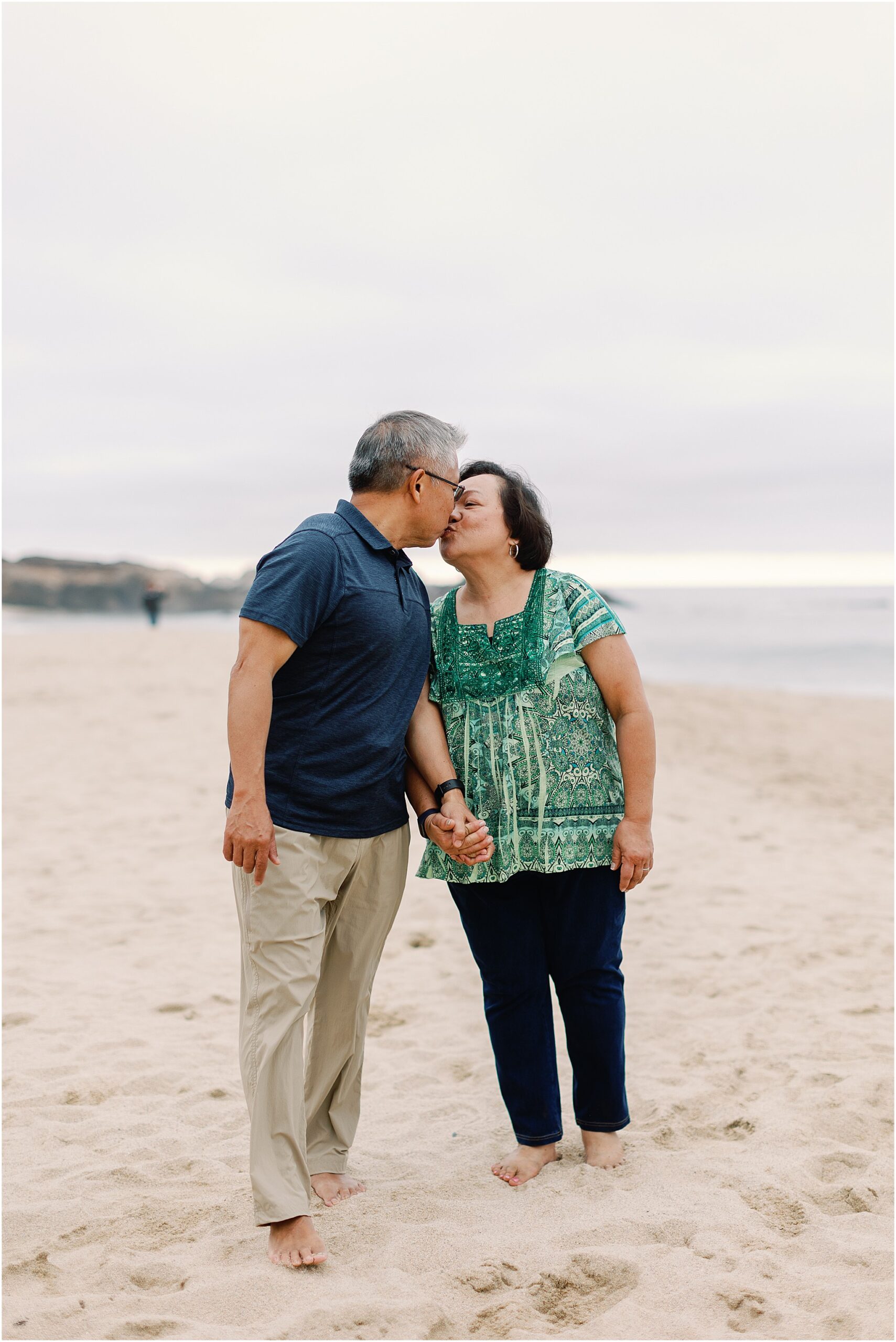 Couple kissing on the Big Sur shoreline with waves in the background.