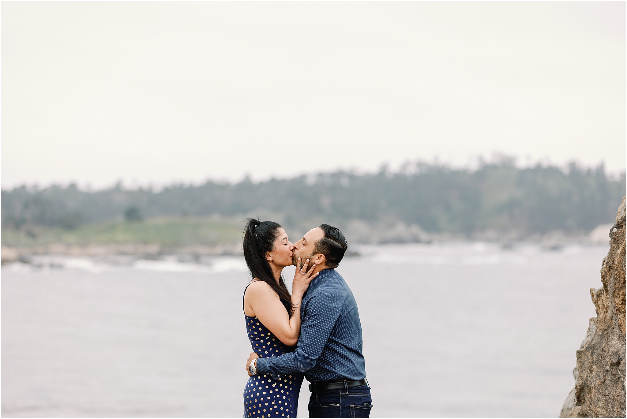The couple kissing with the Carmel coastline behind them.