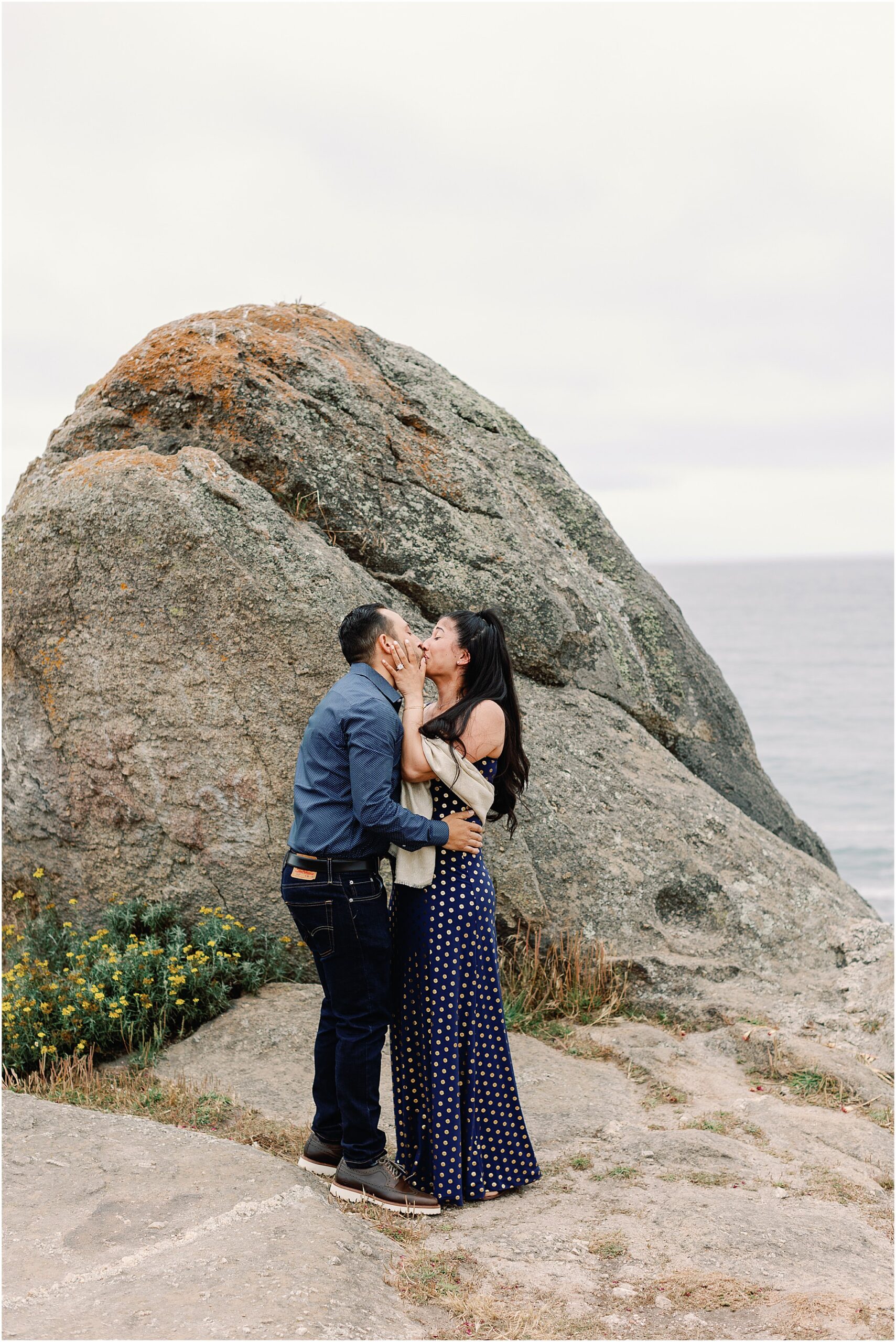 The couple sharing a kiss with waves crashing behind them.