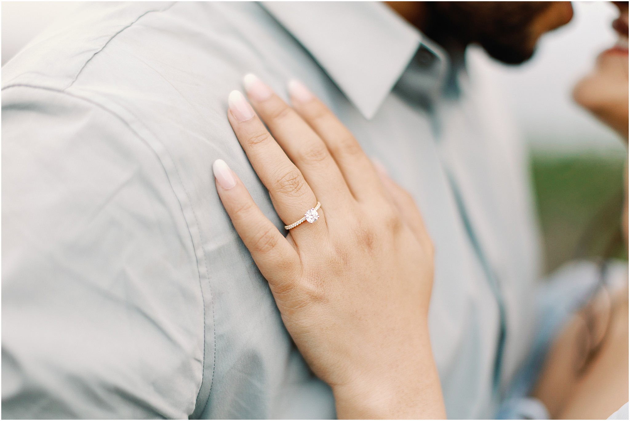 Engagement ring close up on her hand resting on his shoulder during a romantic beach proposal.