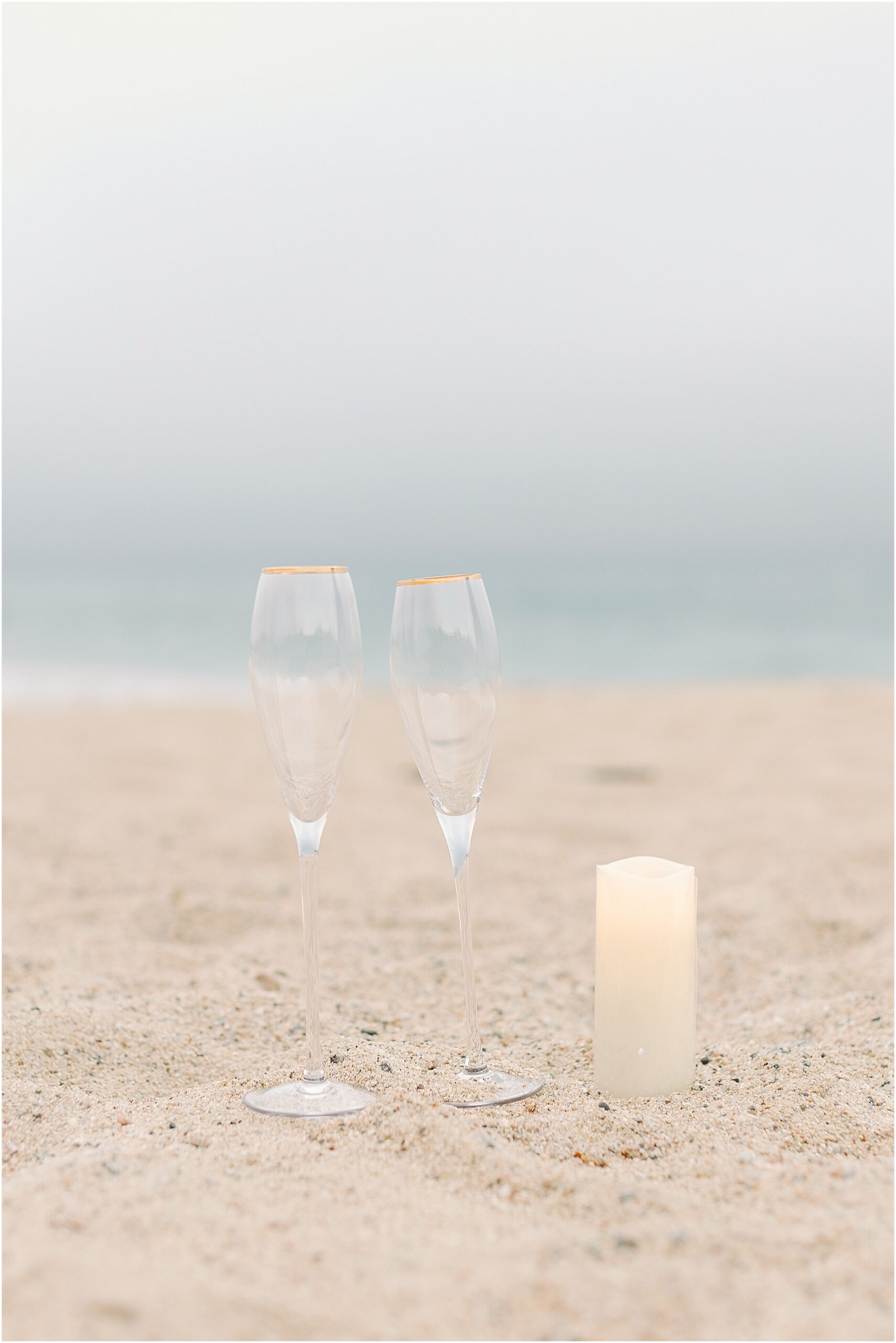 Champagne flutes and candle placed in the sand for a simple and elegant proposal setup.