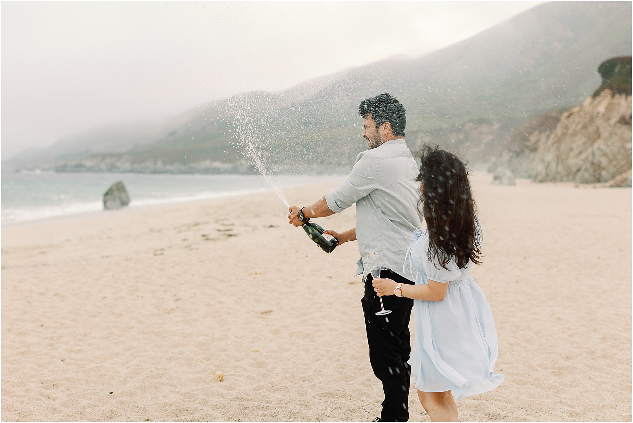 Champagne spray celebration after popping the bottle on the beach during a Big Sur proposal session.