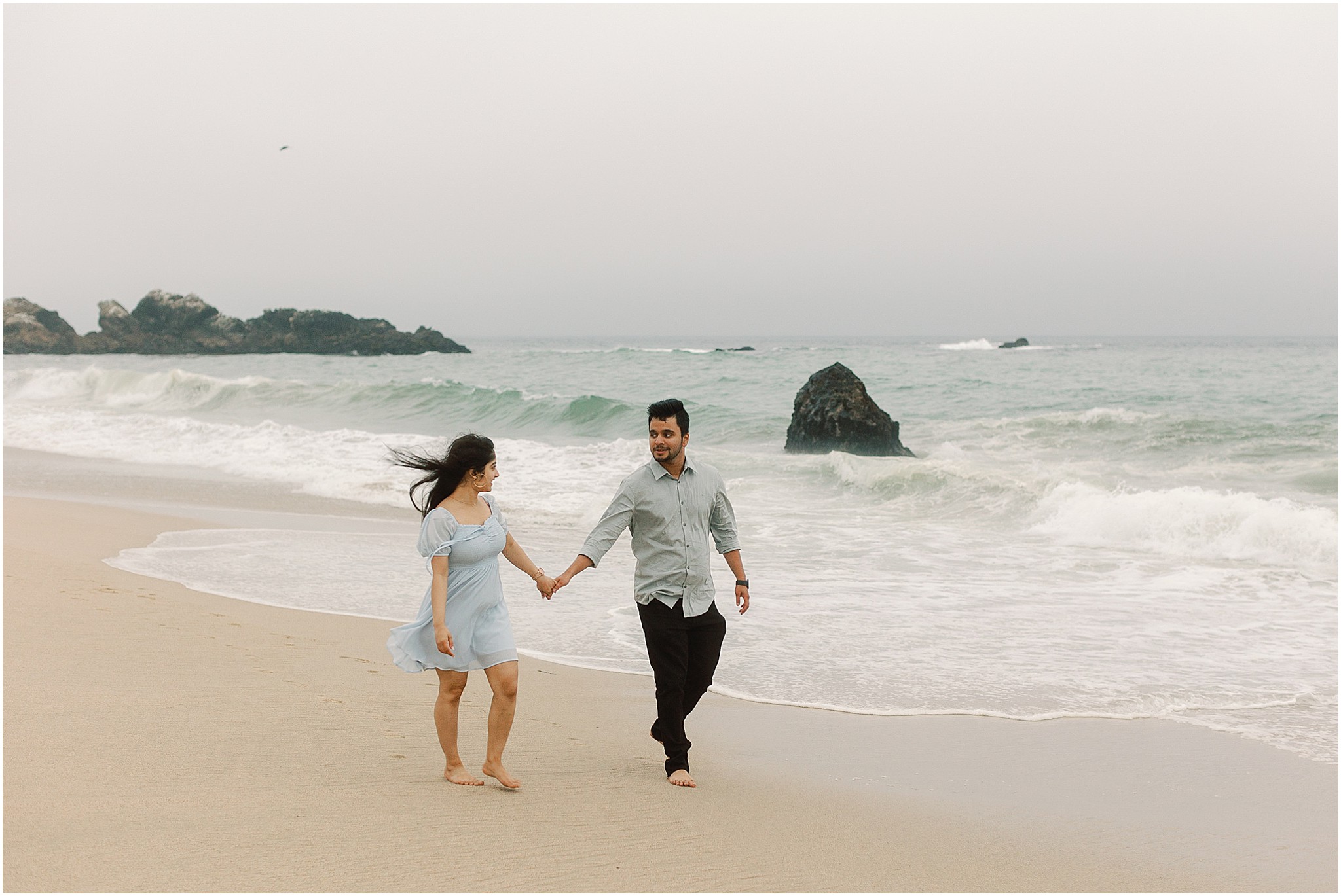 Couple walking barefoot along the shoreline with waves behind them on the Big Sur coast.