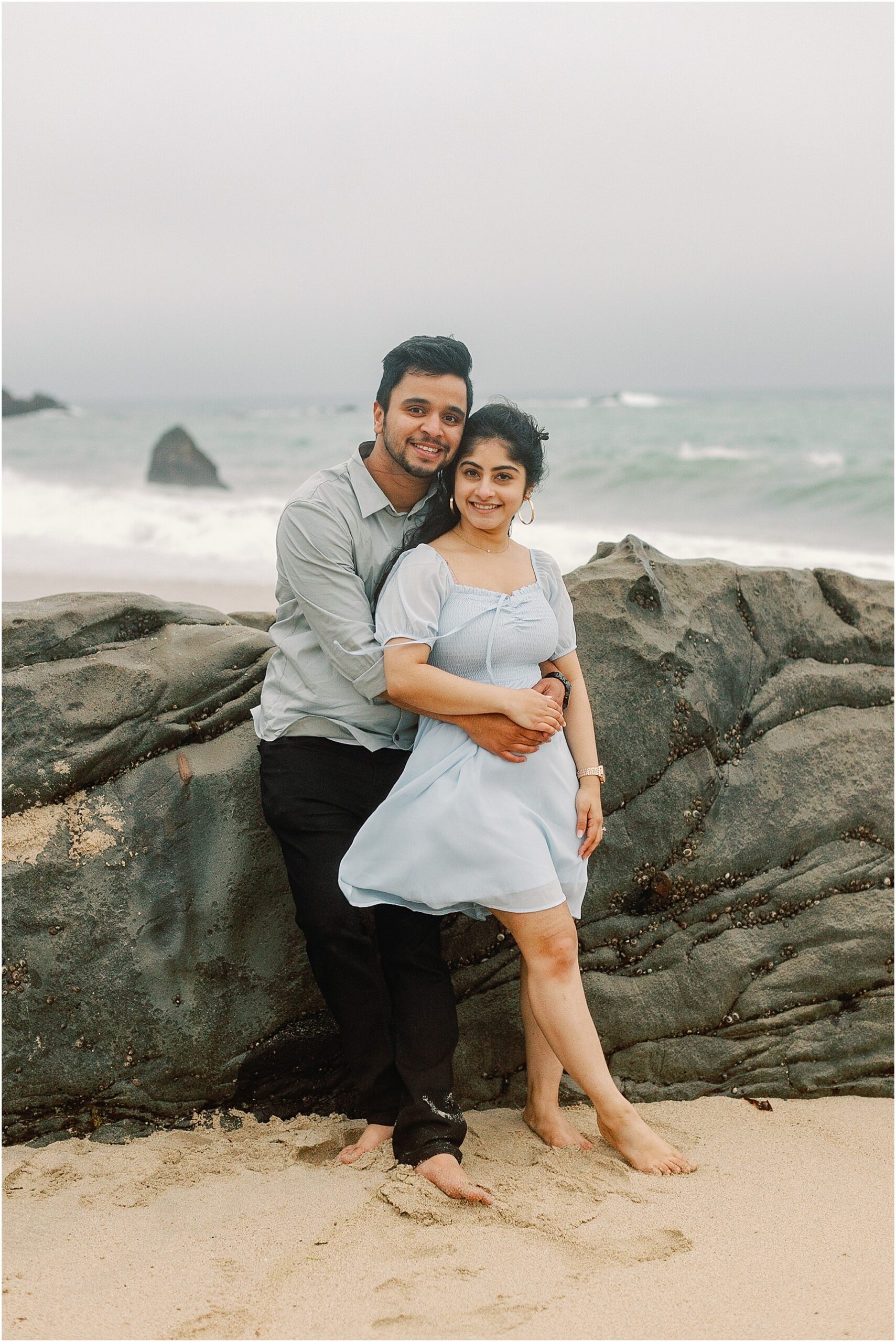 Big Sur coastline proposal moment with couple embracing on the beach in soft foggy light.