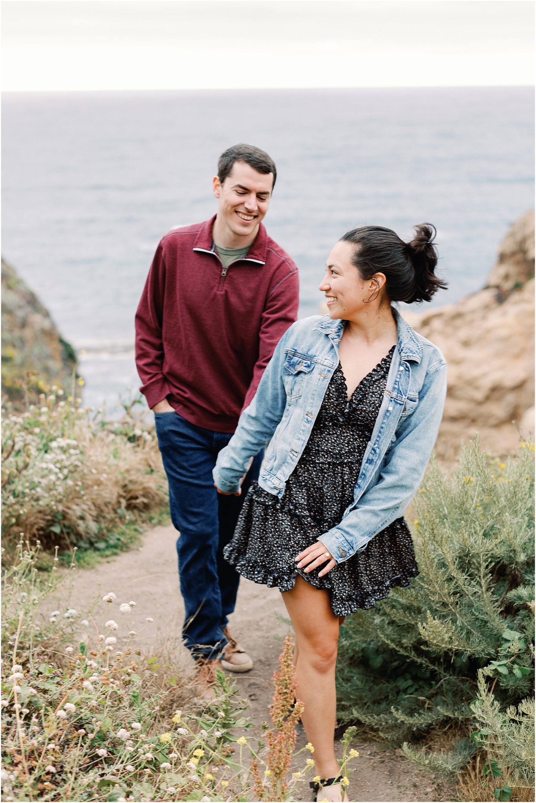 Engaged couple laughing together while walking on a Big Sur coastal trail.
