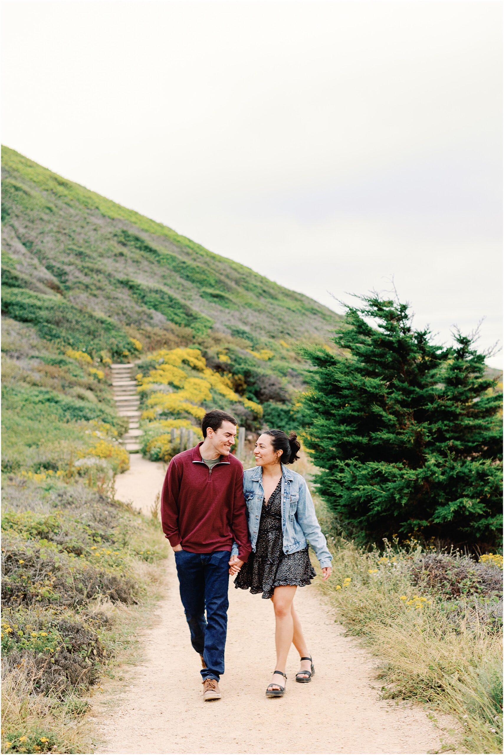 Anna and Ron smiling while walking through wildflowers during Big Sur engagement session