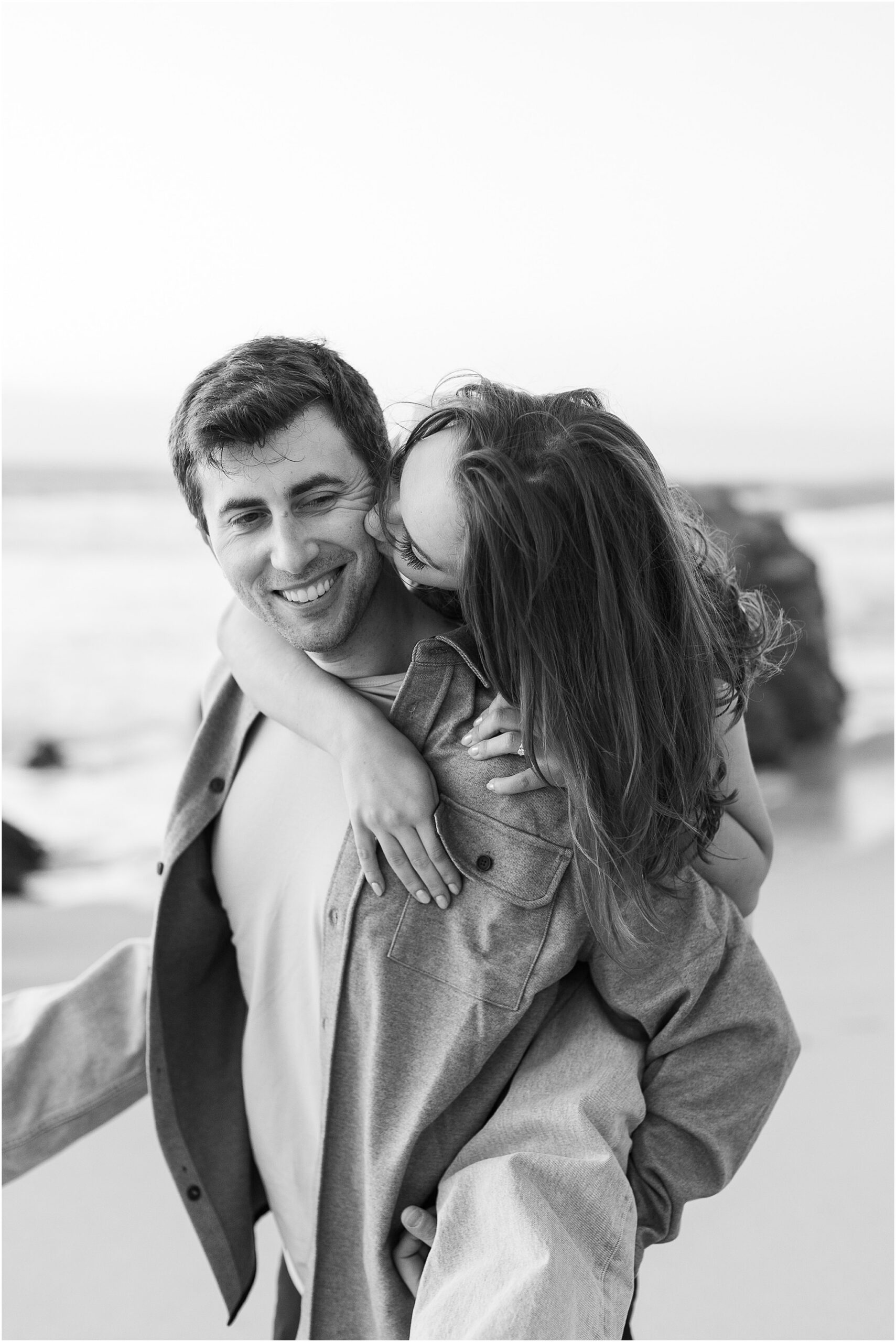 Jenny giving Joey a kiss as waves crash around them during their engagement session