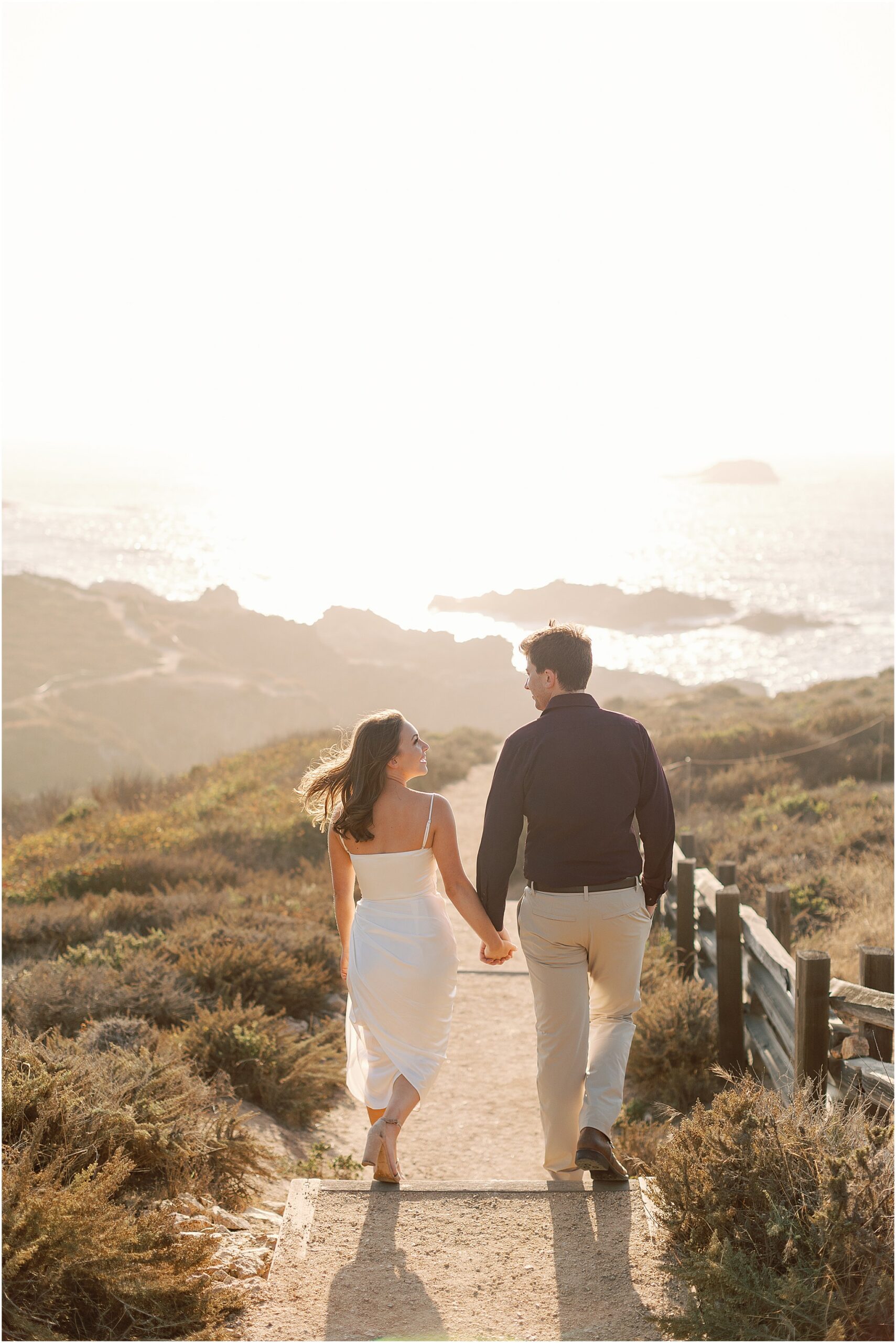 Jenny and Joey walking hand in hand during their coastal engagement session.