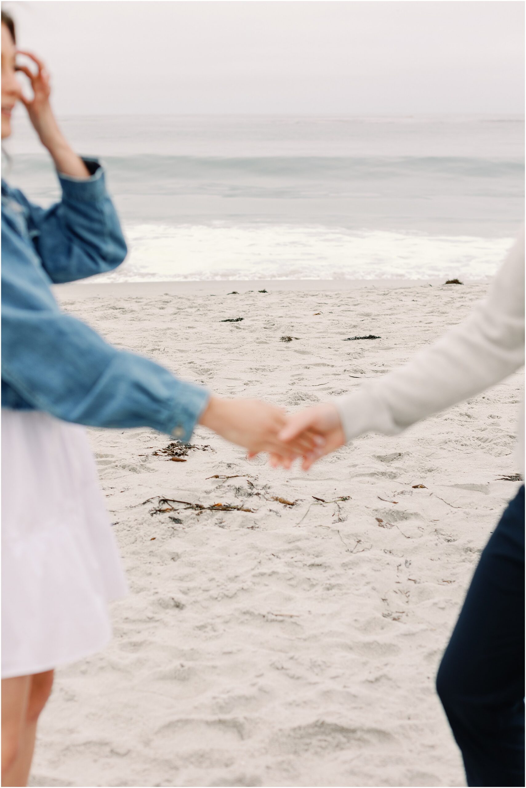 Couple holding hands on Carmel Beach during a surprise proposal