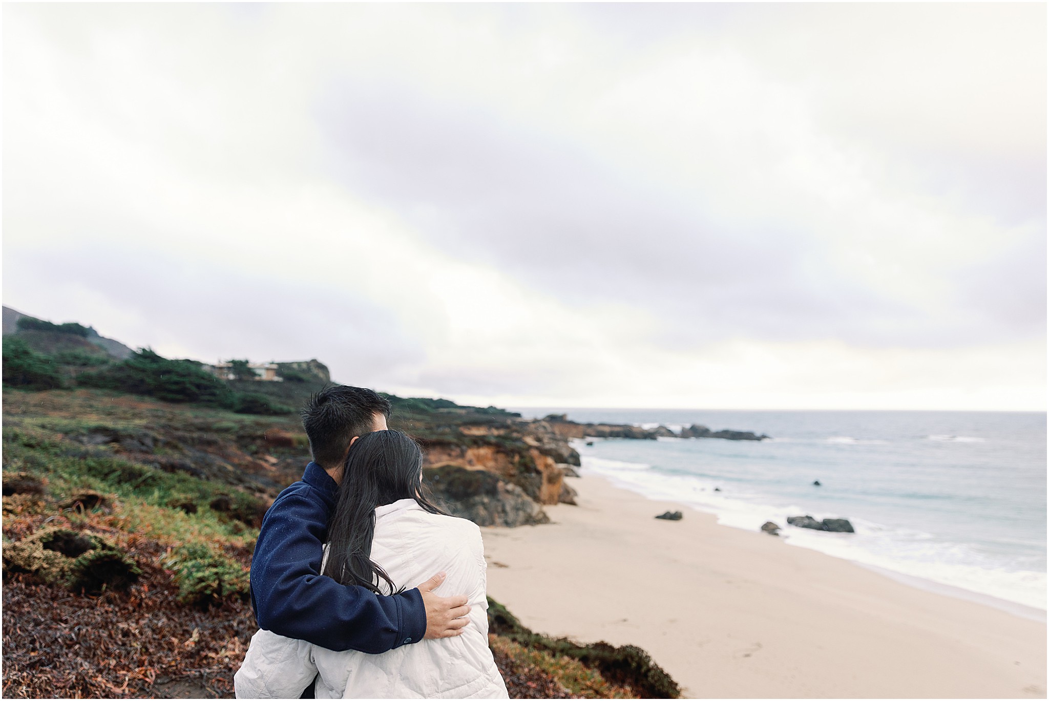 Couple holding each other after engagement on coastal cliff.