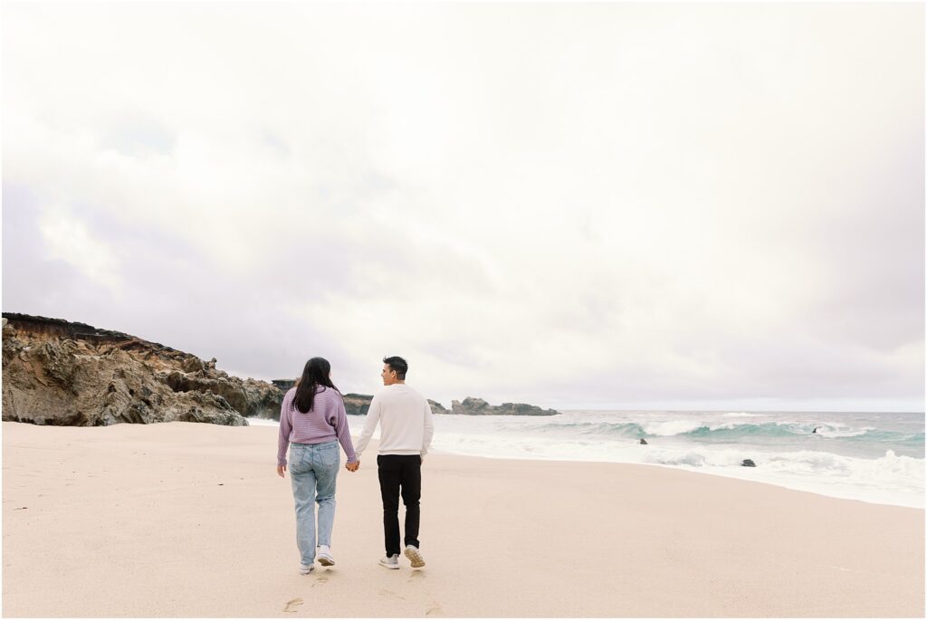 Couple walking together along Big Sur coastline after proposal.