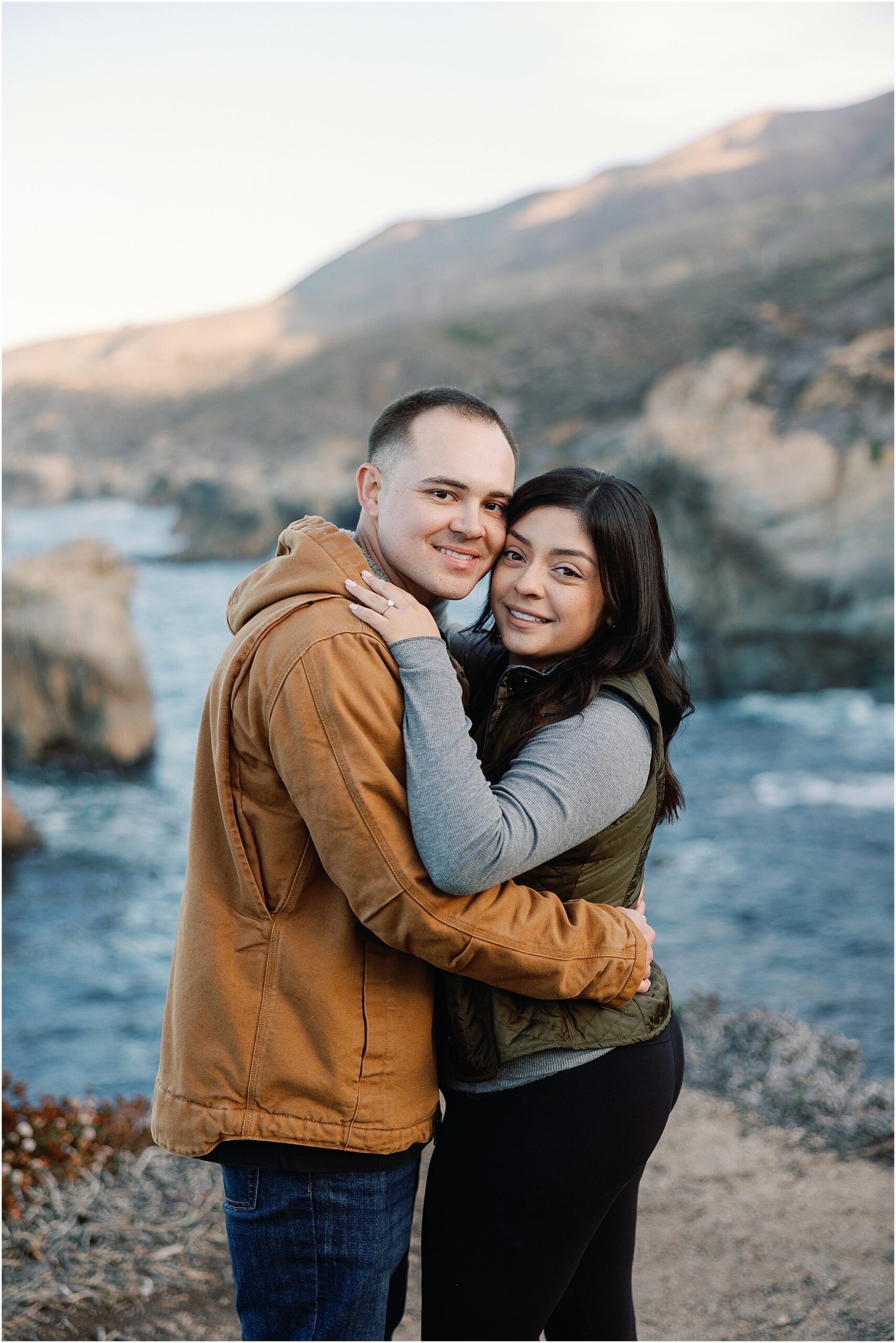 Couple holding each other on scenic Big Sur coastline.