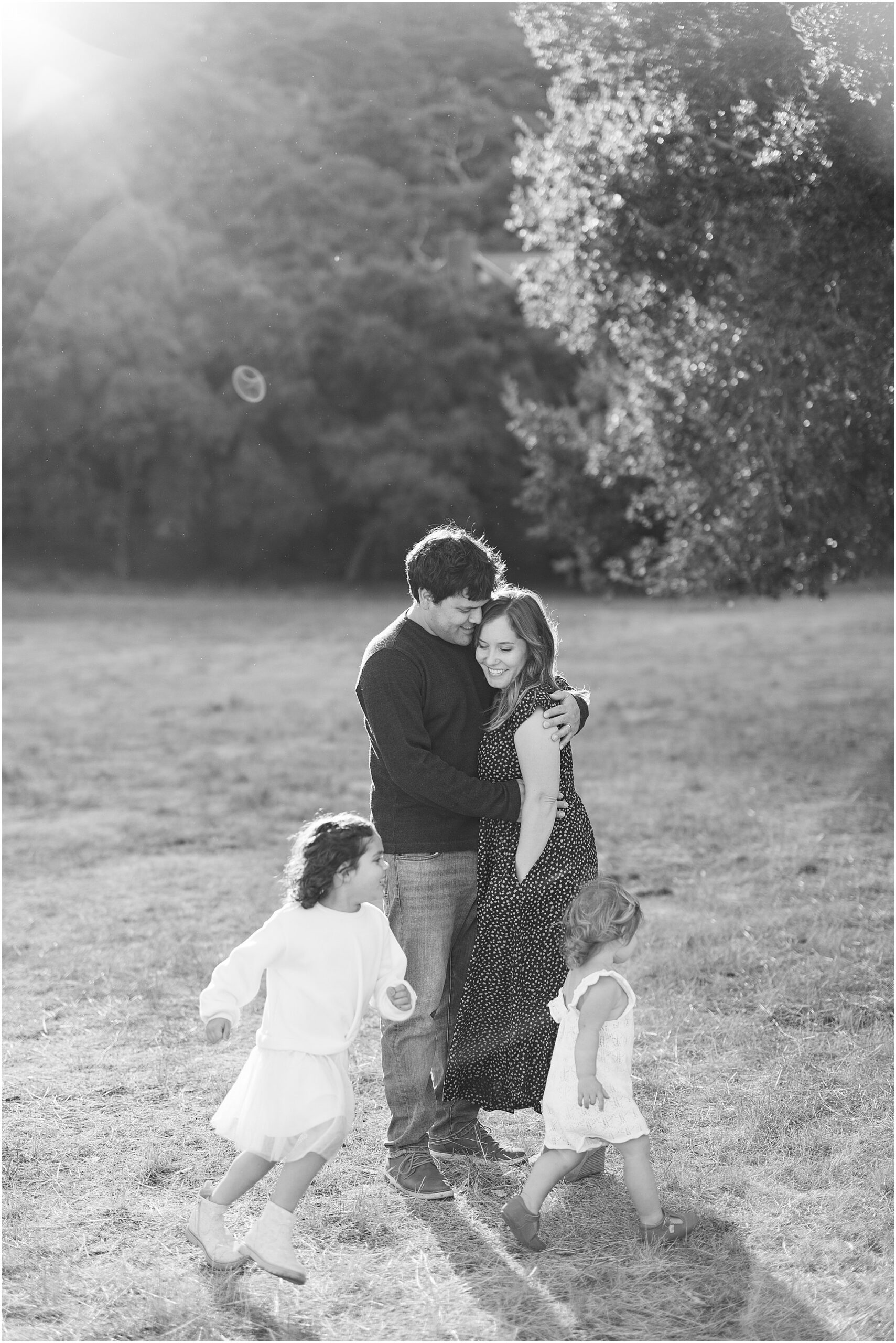 Family and daughters smiling together in natural outdoor setting shot in black and white.
