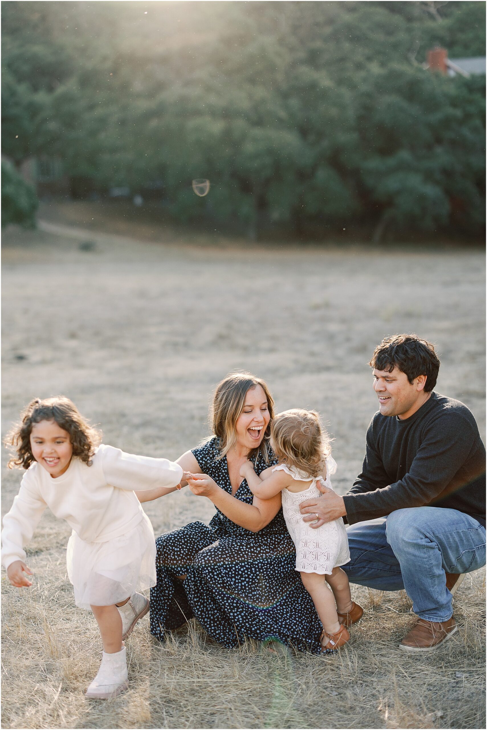 Family of four laughing in golden field in Monterey County during sunset.