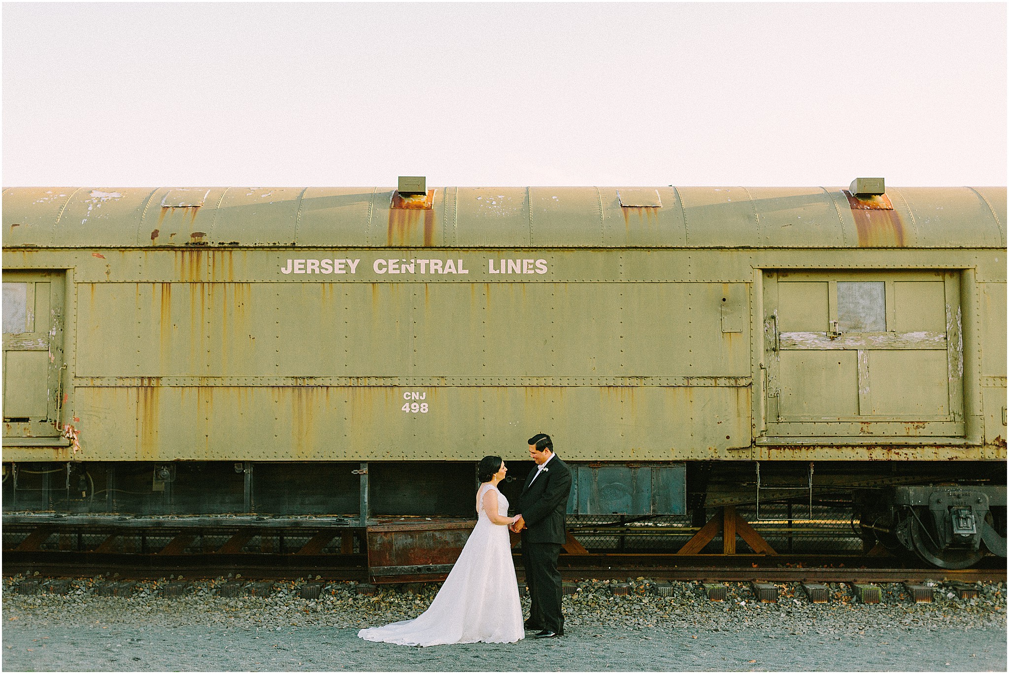 Bride and groom posing in front of vintage train car during unique Philadelphia wedding portraits