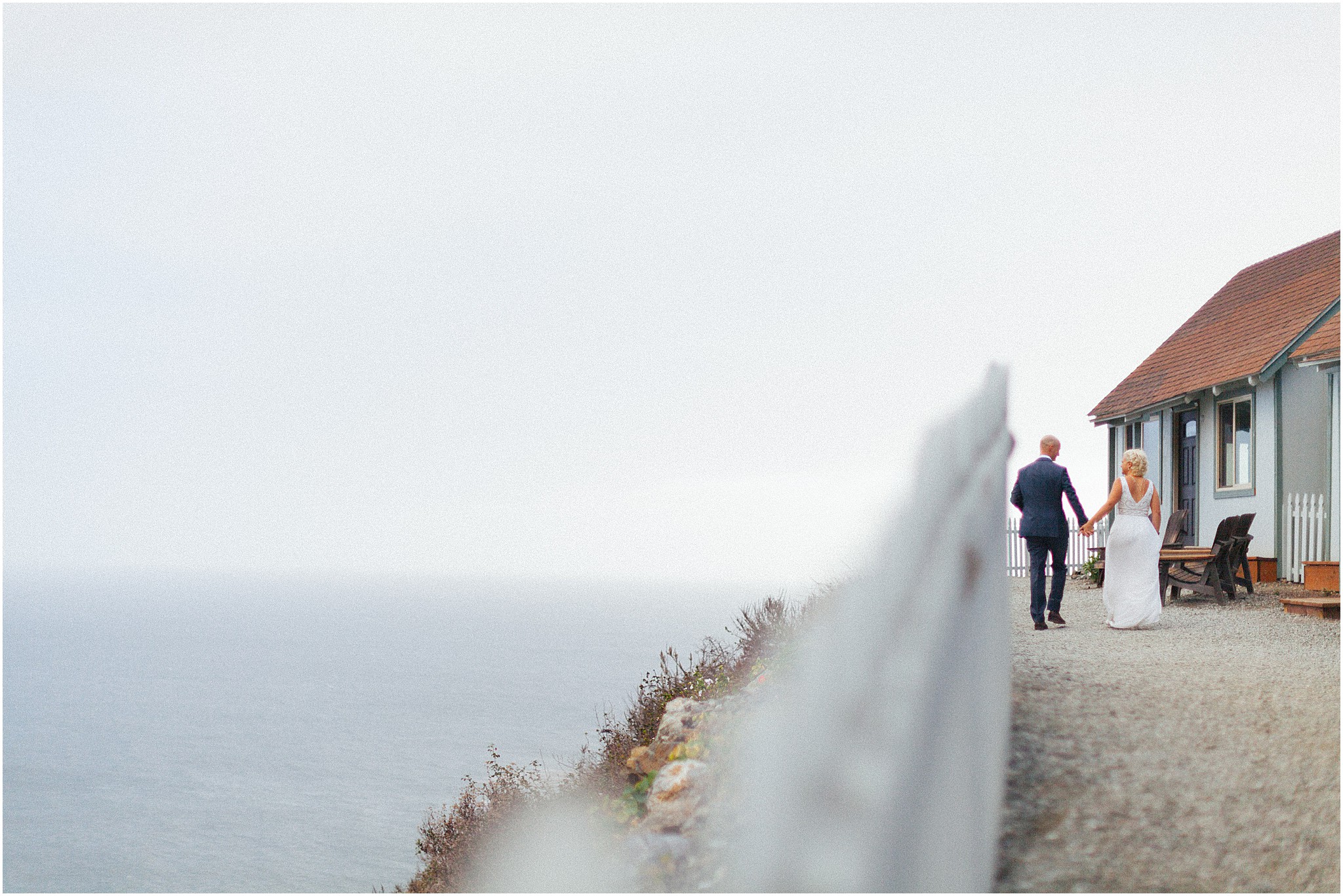 Bride and groom walking together along Big Sur coastline.