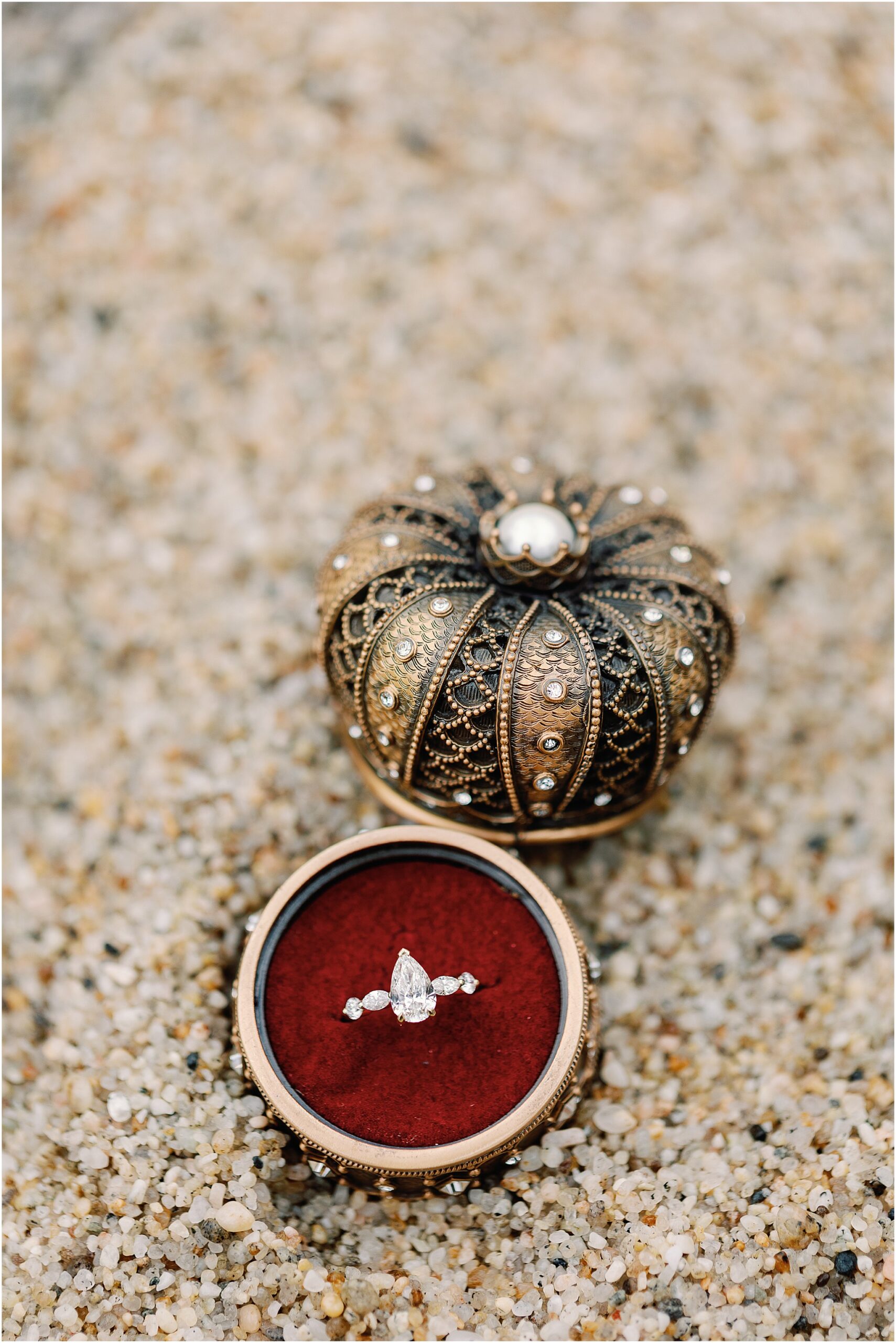 Pear shaped engagement ring in an ornate ring box on the sand at Pebble Beach