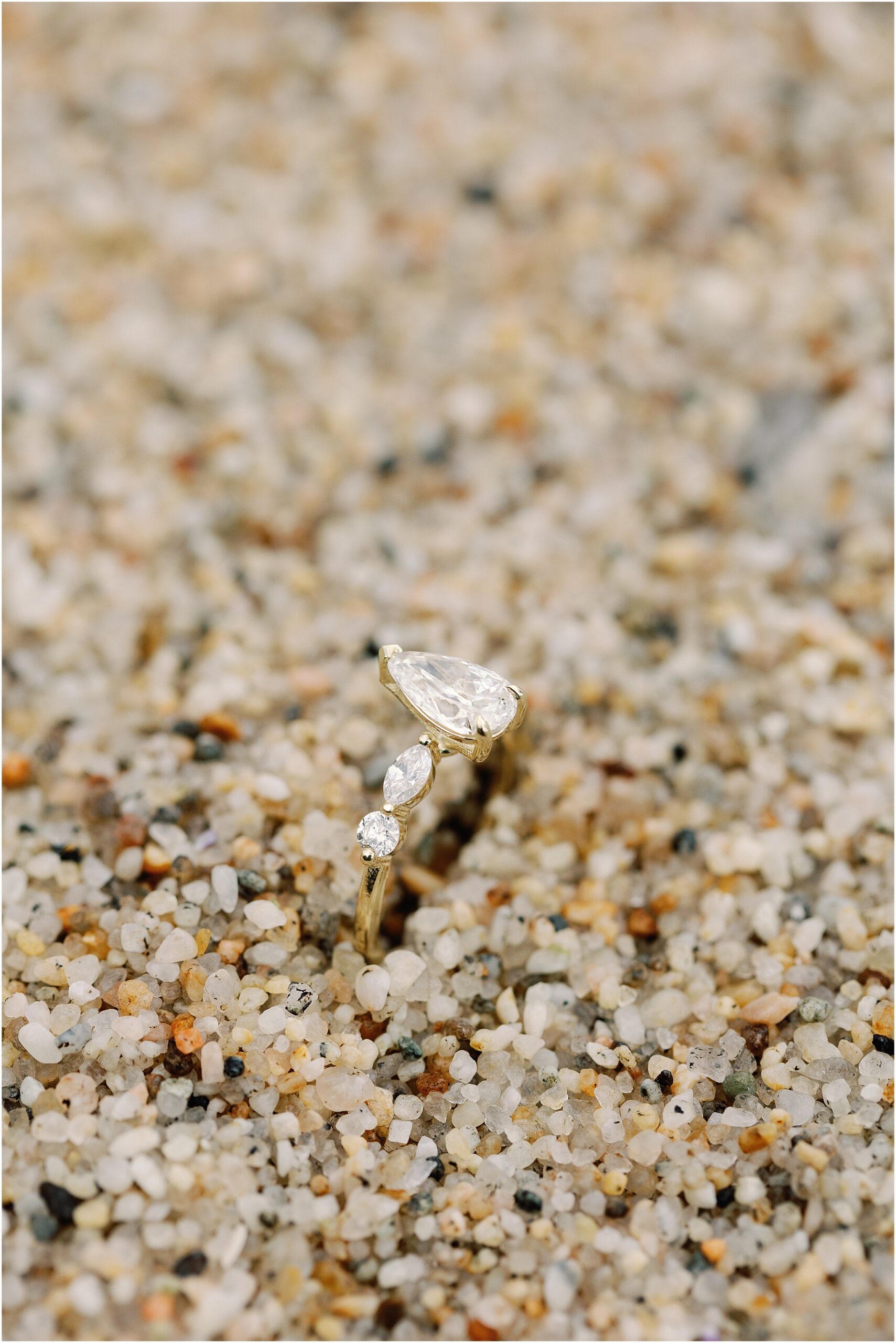 Close up of Ivery’s pear shaped yellow gold engagement ring photographed in the sand at Pebble Beach