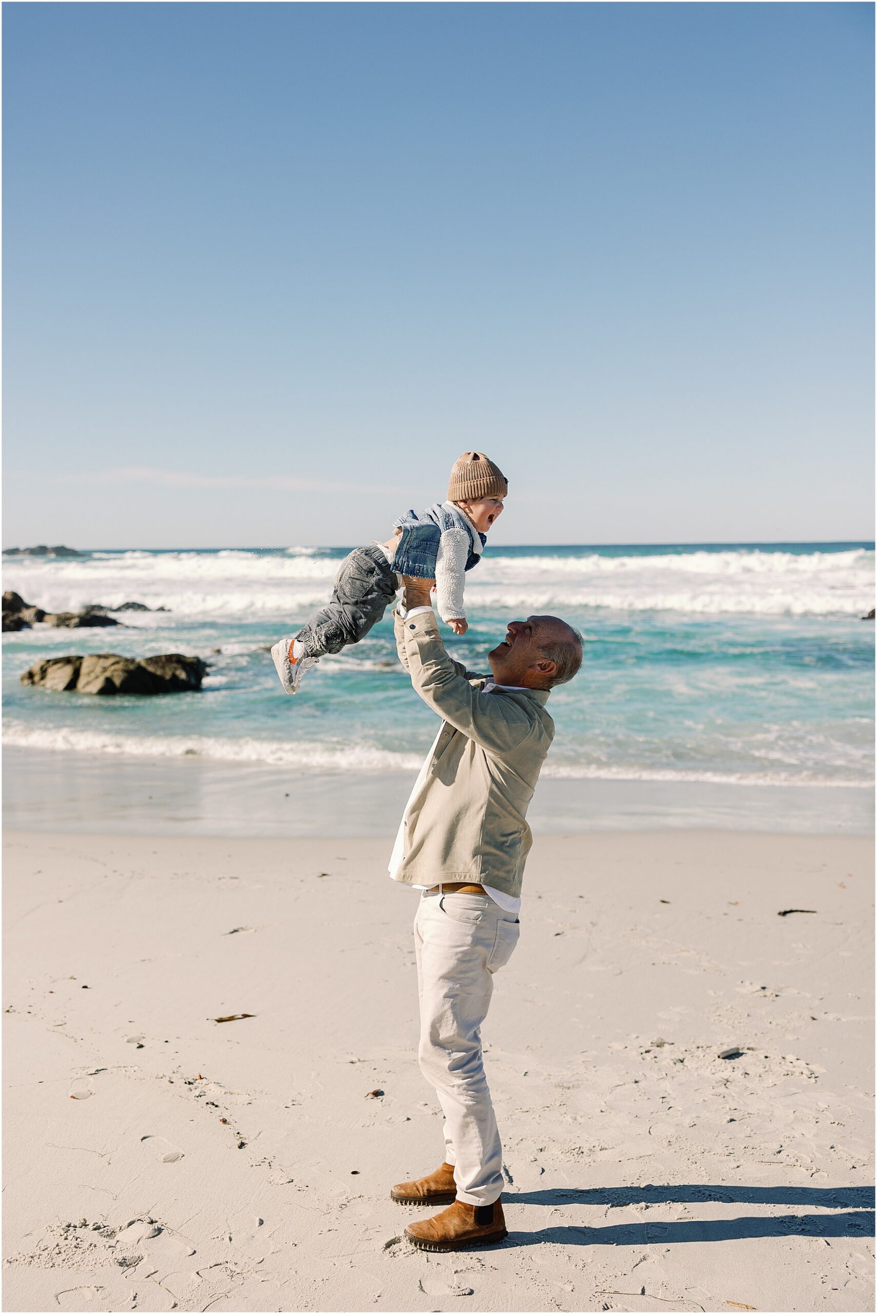 Grandfather lifting his grandson into the air on the beach along the Carmel Coast