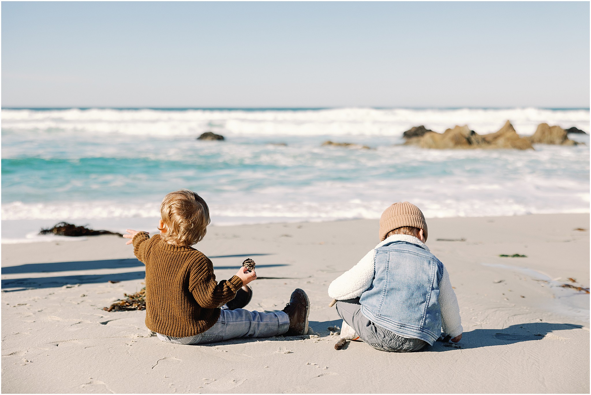 Two young children exploring the beach with their parents along the Carmel Coast